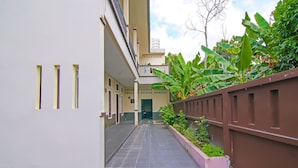 A corridor with a tiled floor, a brown wall with a planter, and a building entrance. - Hotel O Putri Guest House Syariah Near SPBU Rimbo Panjang (Pekanbaru)