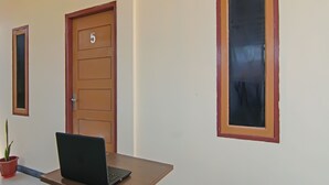 A room with a laptop on a table, a door with the number 5, and a window with a red frame. - Hotel O Putri Guest House Syariah Near SPBU Rimbo Panjang (Pekanbaru)