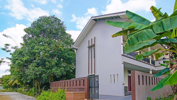 A modern two-story house with a gated entrance, surrounded by lush greenery and a large tree. - Hotel O Putri Guest House Syariah Near SPBU Rimbo Panjang (Pekanbaru)