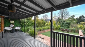 A covered outdoor area with a wooden deck, two round wicker chairs, and a dining table with chairs.