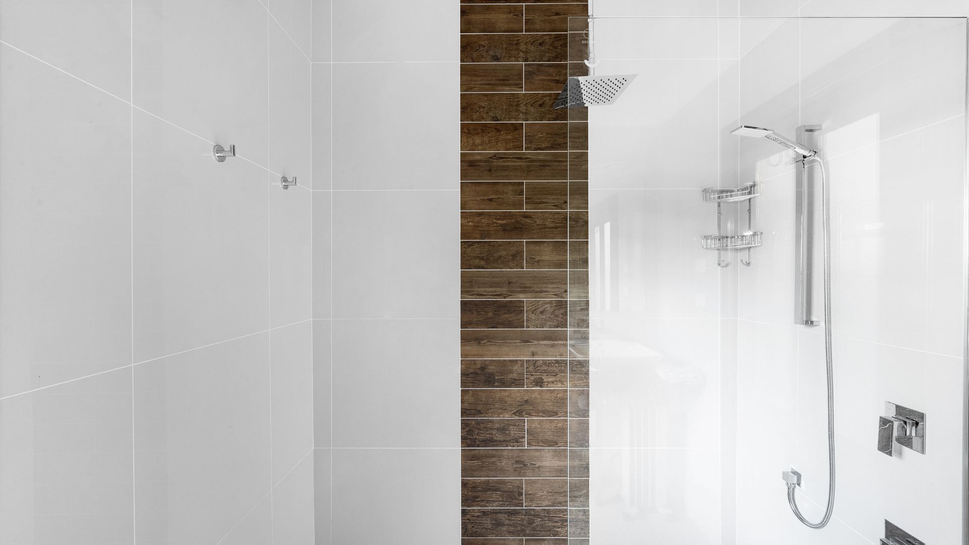 A modern bathroom with white tiles, a wooden accent wall, and a glass shower enclosure.