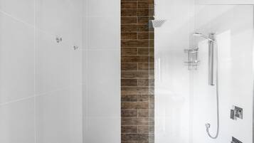 A modern bathroom with white tiles, a wooden accent wall, and a glass shower enclosure.