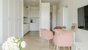 A modern kitchen with white cabinets, a dining area with a round table and pink chairs, and a chandelier. - RentPlanet - Apartamenty Zajezdnia (Wroclaw)