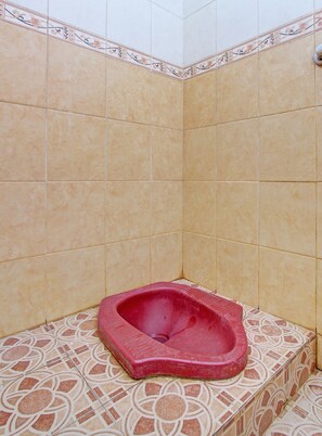 Een badkamer met beige betegelde wanden en vloer, een rood toilet en vloertegels met een patroon.