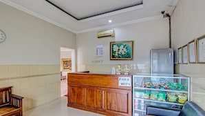 Ein Empfangsbereich mit Holztresen, einer Uhr, einem gerahmten Blumenbild, einem Kühlschrank und einer Snackauslage.