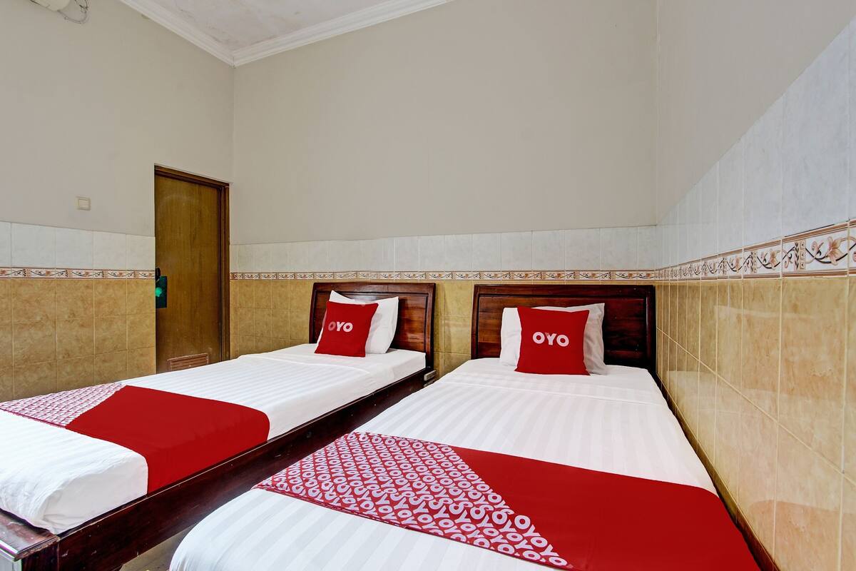 Twee enkele bedden met rode en witte beddengoed, een houten hoofdbord en een betegelde muur met decoratieve rand.