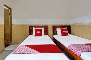 Zwei Einzelbetten mit roter und weißer Bettwäsche, ein hölzernes Kopfende und eine geflieste Wand mit dekorativer Bordüre.