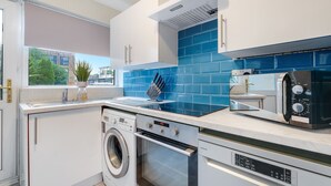 A modern kitchen with a washing machine, oven, and microwave. - Bourne Court Attractive 1 bdrm Apartment (Ruislip)