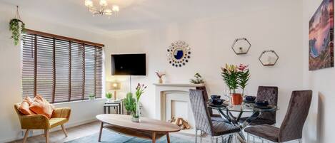 A modern living room with a sofa, dining table, chairs, a fireplace, and decorative wall art.