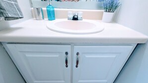 Un meuble-lavabo blanc pour la salle de bain, doté d’un évier, de deux portes et d’un miroir.