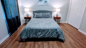 Une chambre à coucher avec un grand lit, deux tables de chevet, un tableau abstrait accroché au mur et une porte blanche.