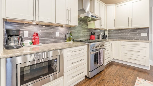 A modern kitchen with white cabinets, stainless steel appliances, and a tiled backsplash. - Modern, Walkable Family Home w/ Porch & Parking (Atlanta)
