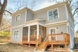 A two-story house with a covered porch, a front door, and a small deck.