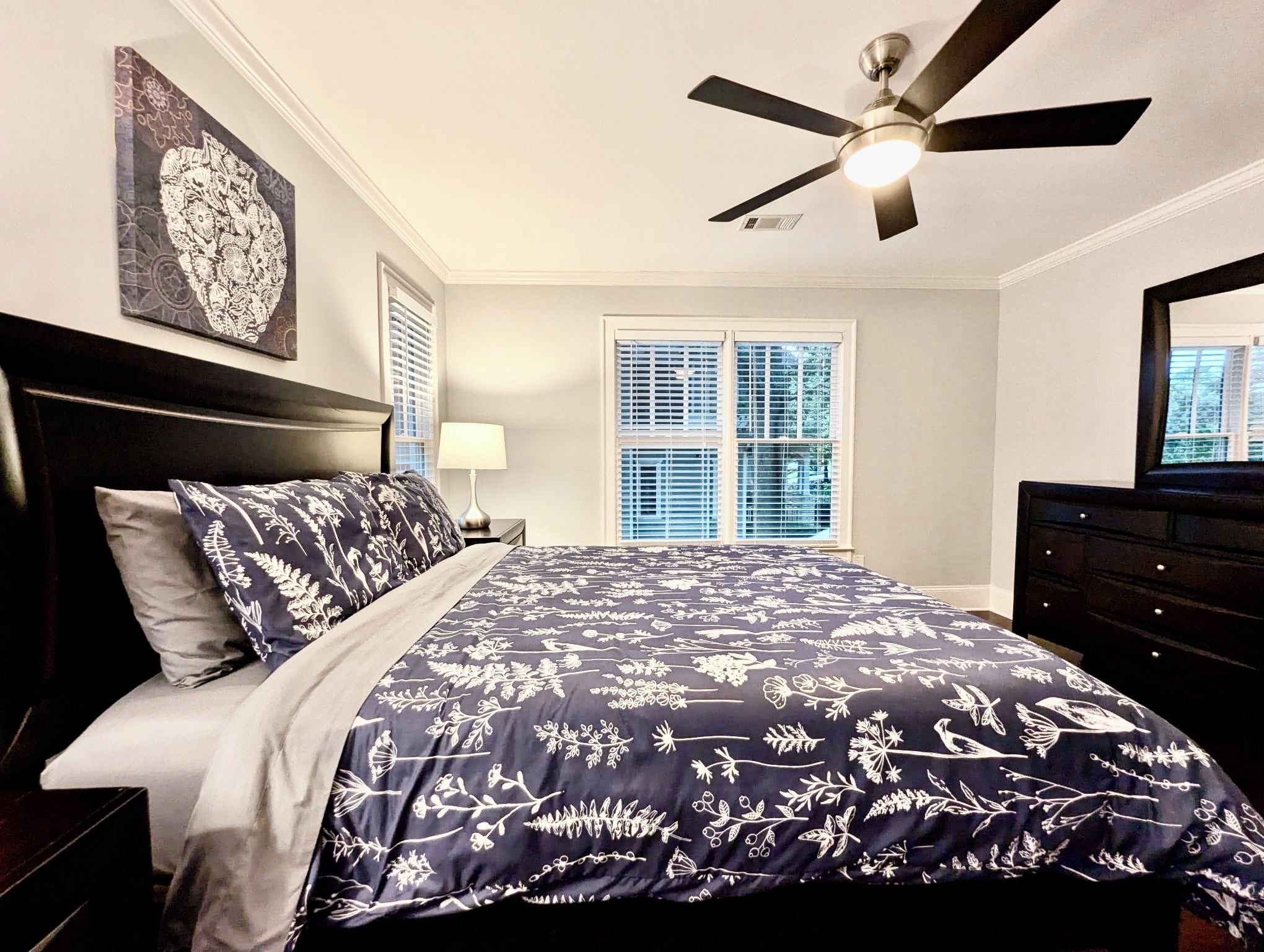 A bedroom with a bed, a ceiling fan, a window with blinds, and a dresser.