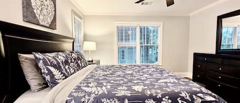 A bedroom with a bed, a ceiling fan, a window with blinds, and a dresser.
