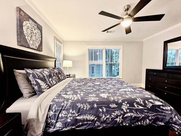 A bedroom with a bed, a ceiling fan, a window with blinds, and a dresser.