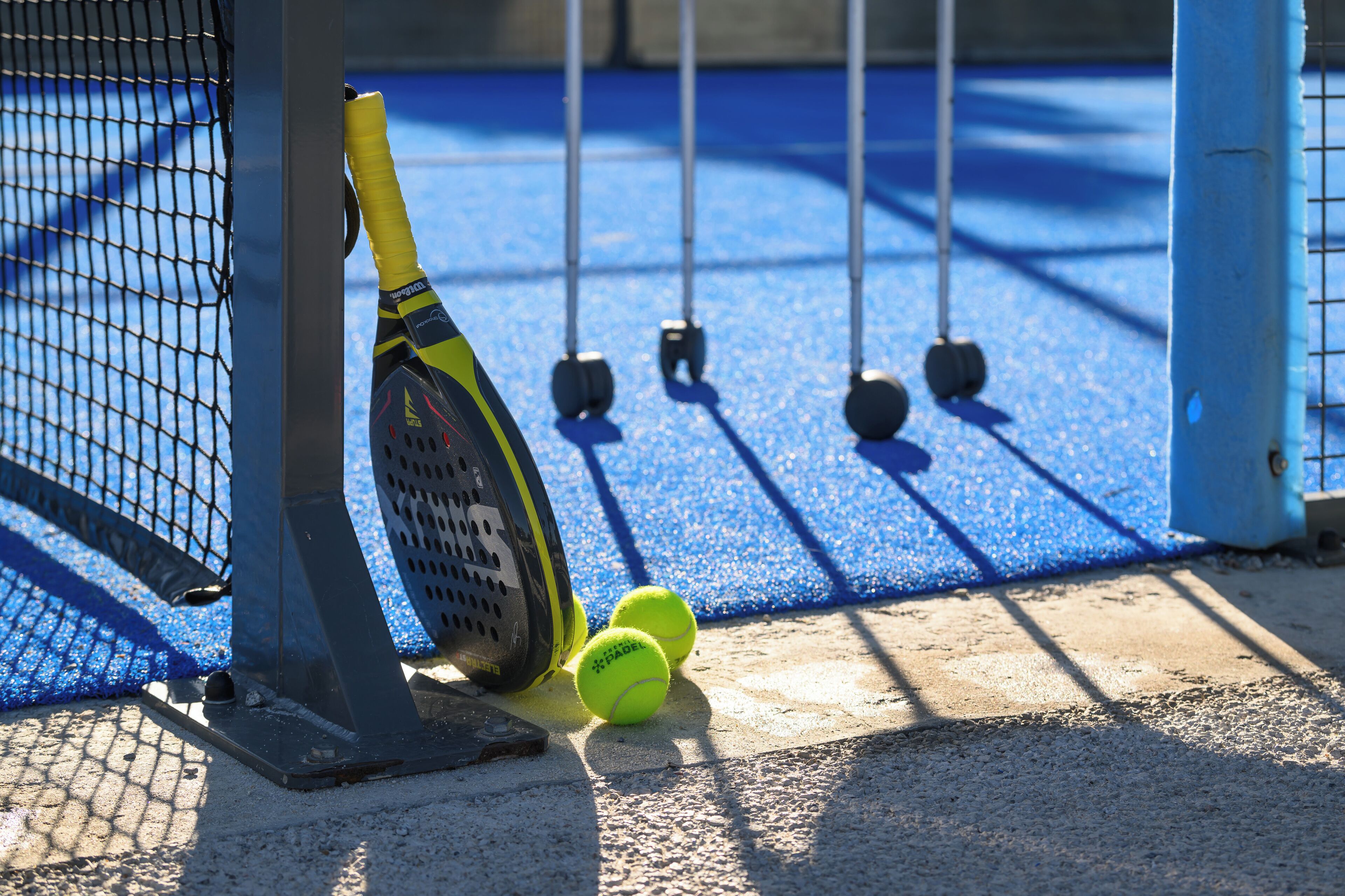 A tennis court with a net, a tennis racket leaning against the net, and two tennis balls on the ground.