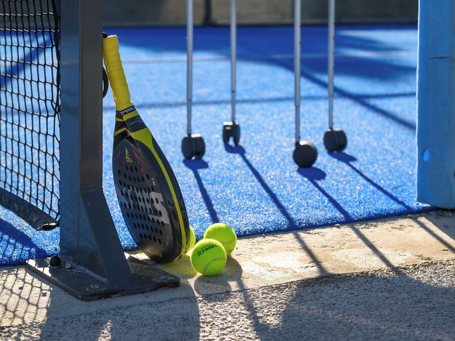 A tennis court with a net, a tennis racket leaning against the net, and two tennis balls on the ground.