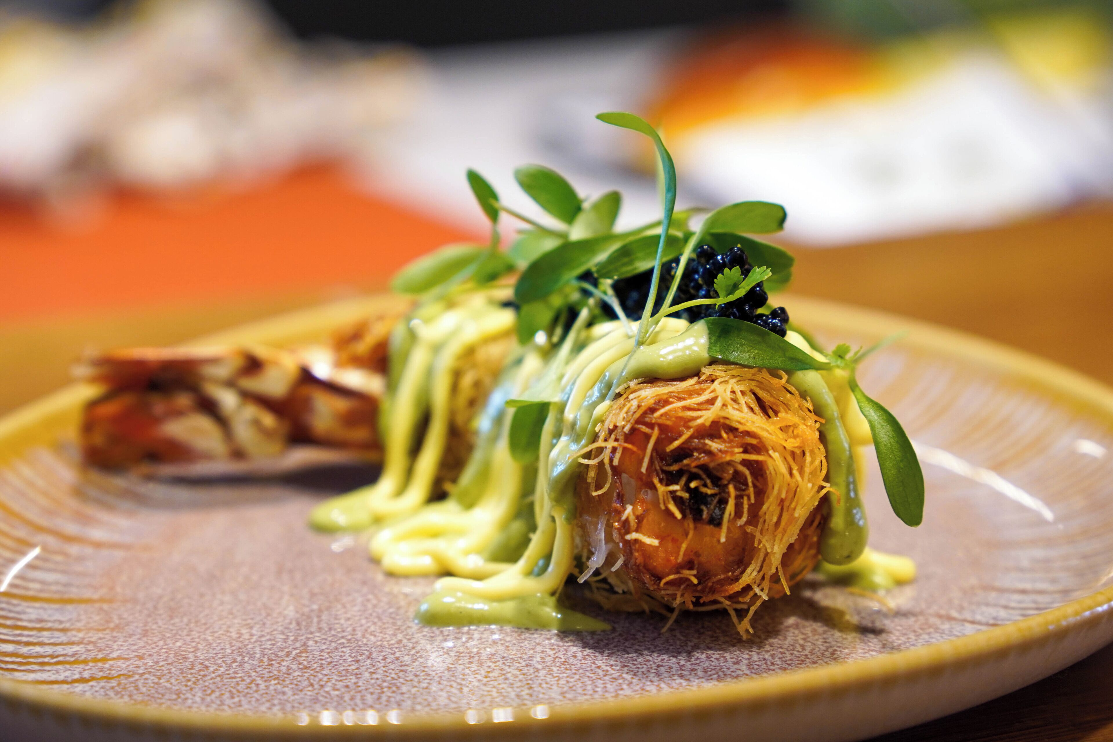 A plate with a rolled food item, garnished with green leaves and a creamy sauce.