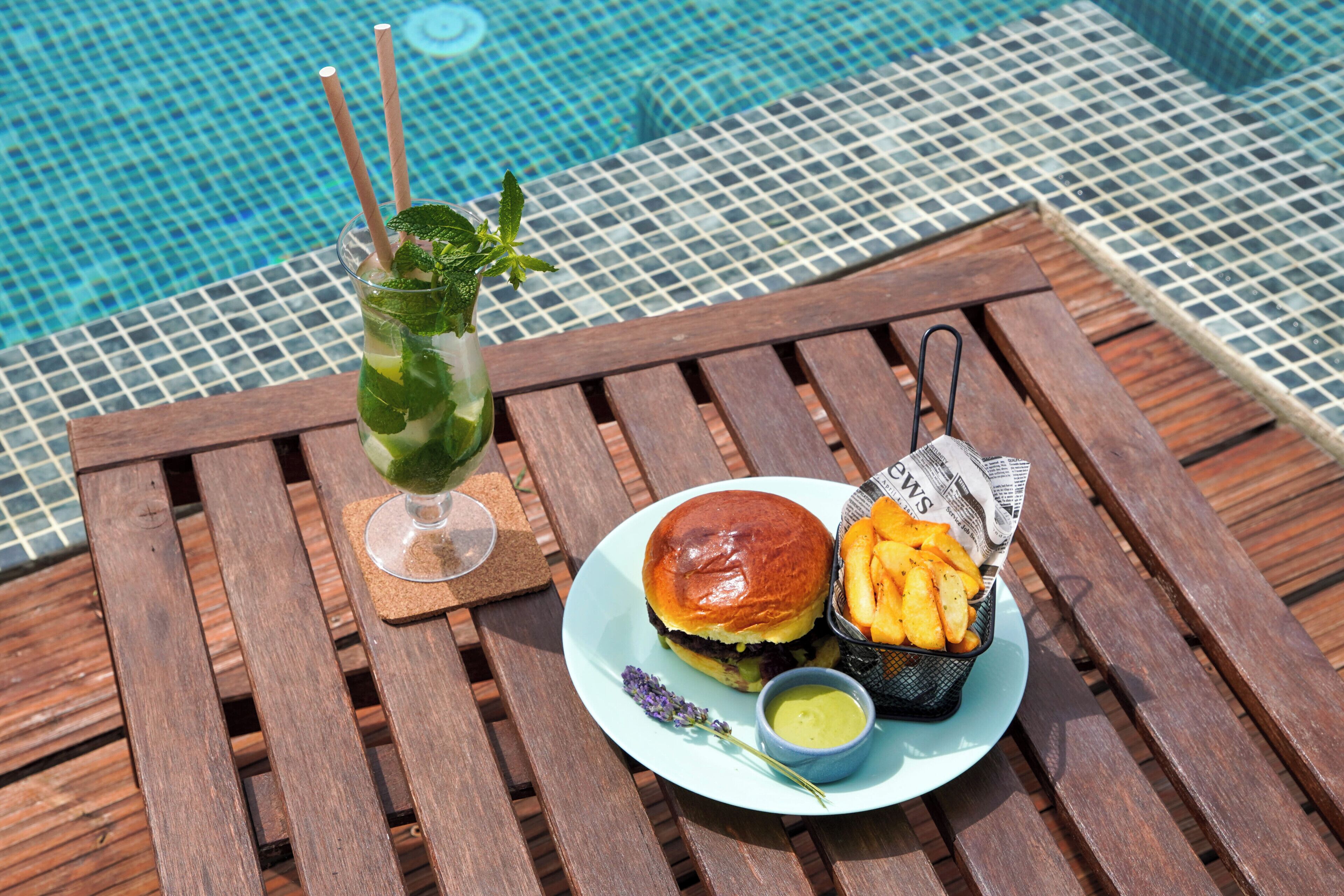 A wooden table with a plate of food, a drink, and a newspaper.