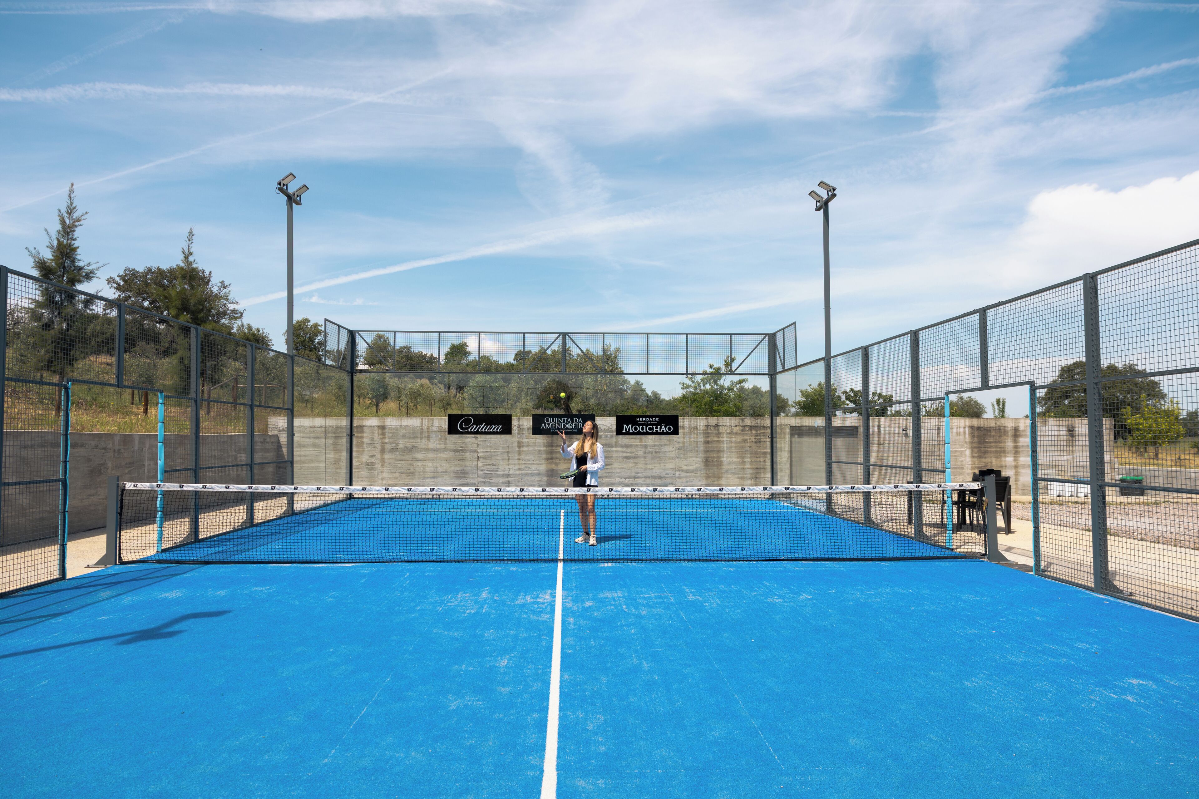 A tennis court with a net, surrounded by fencing, and a few trees in the background.