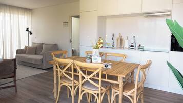 A dining area with a wooden table and chairs, a kitchen with white cabinets, and a living room with a sofa and a lamp.