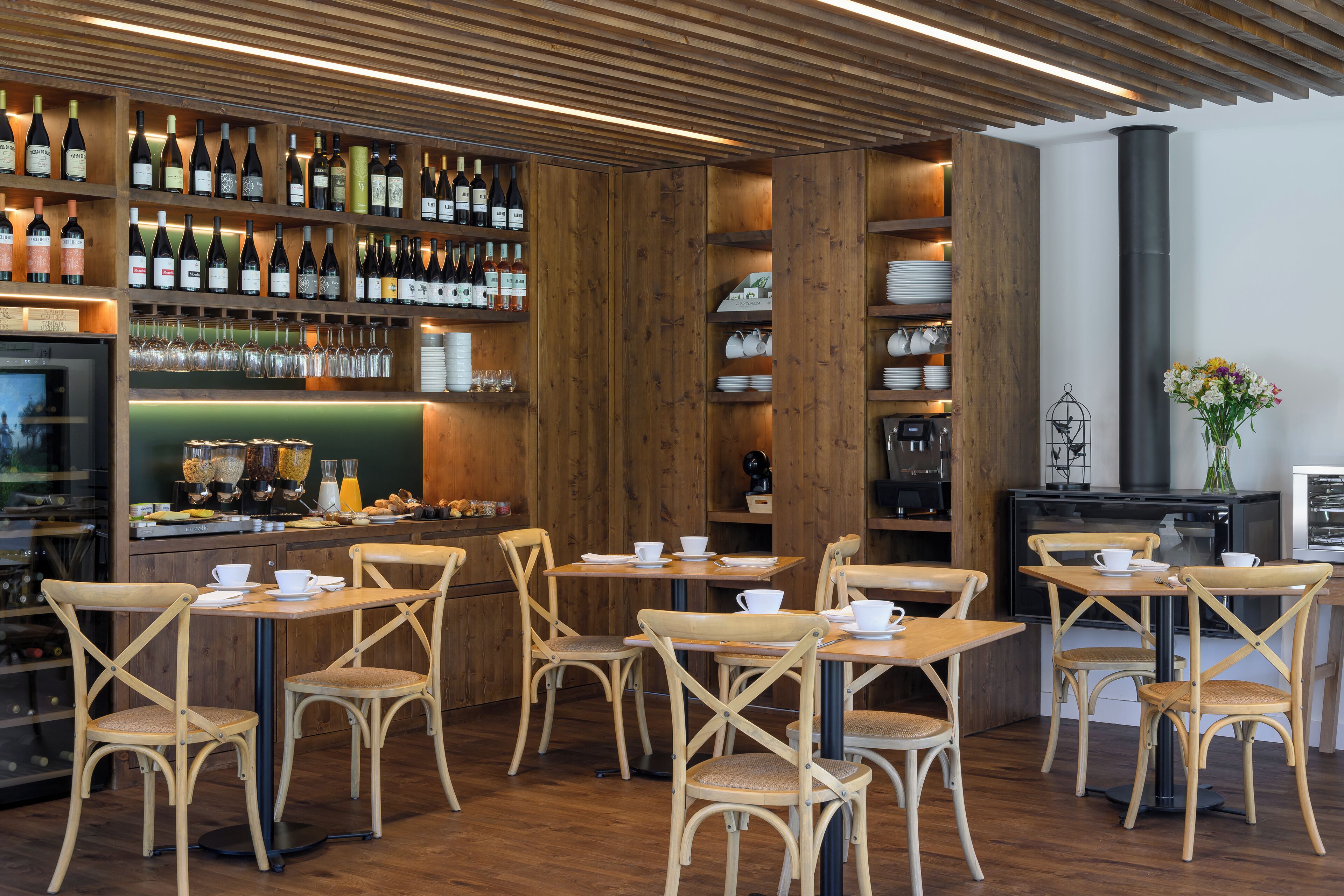 A restaurant with wooden furniture, a bar area with wine bottles, and a coffee machine.
