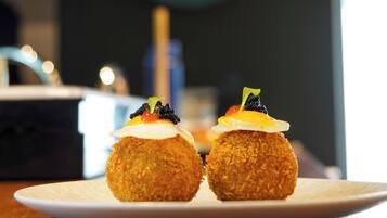 A plate with two round, breaded items topped with a sauce and garnish, on a white plate.