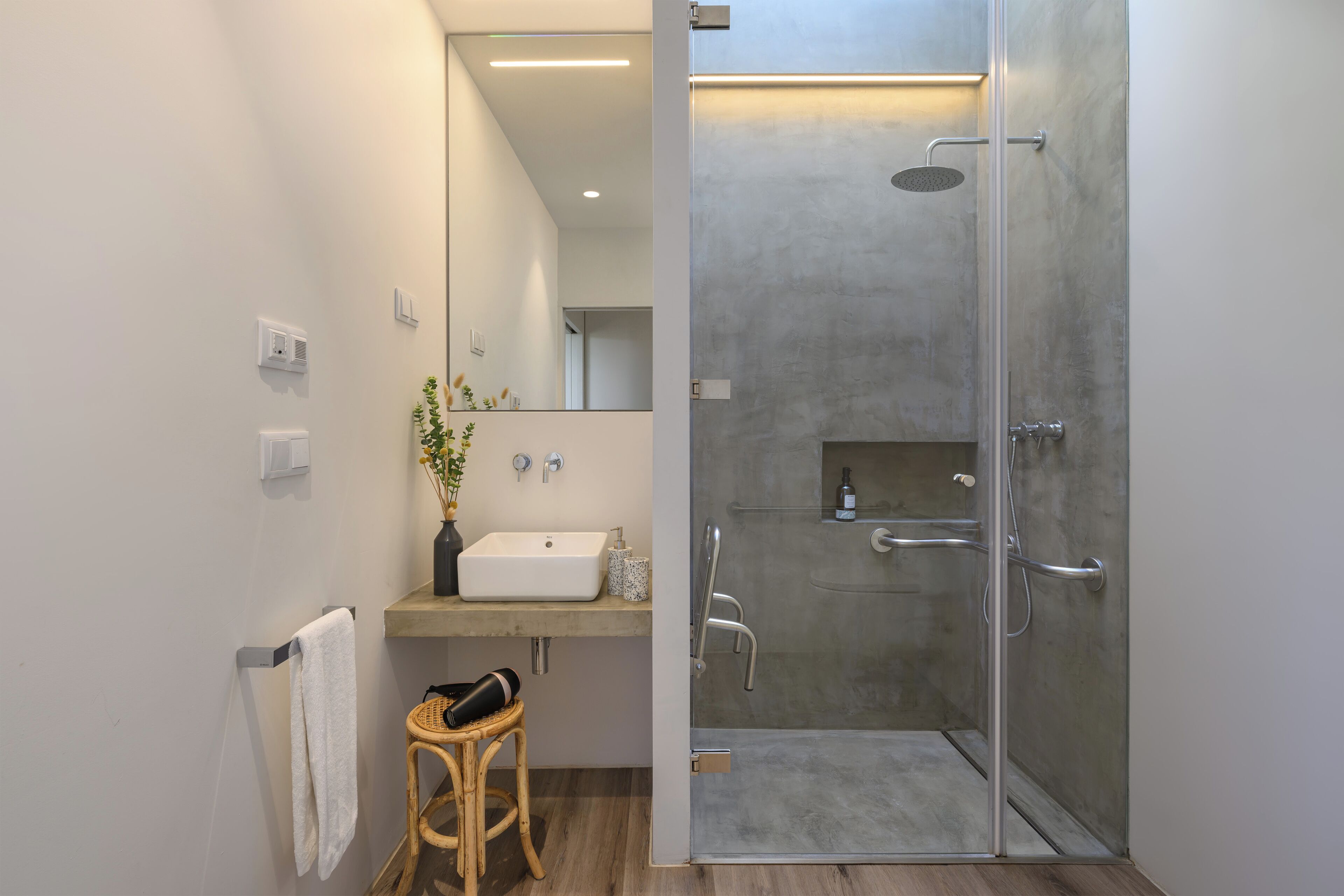 Ein modernes Badezimmer mit einer in Glas eingefassten Dusche, einem Waschbecken mit Blumen in einer Vase und einem hölzernen Hocker.