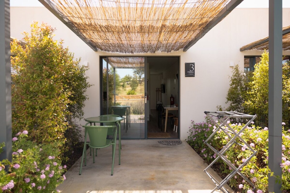 Een terras buiten met een tafel en stoelen, een deur naar binnen en een metalen wasrek.
