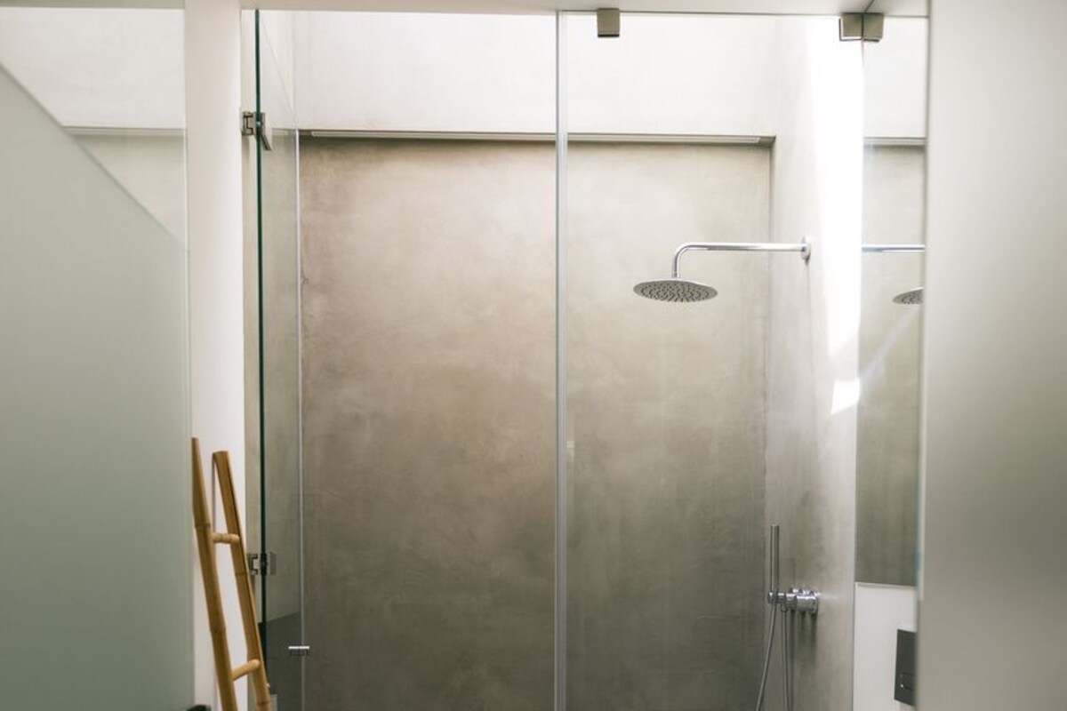 A modern bathroom with a glass-enclosed shower, a toilet, and a wooden ladder.