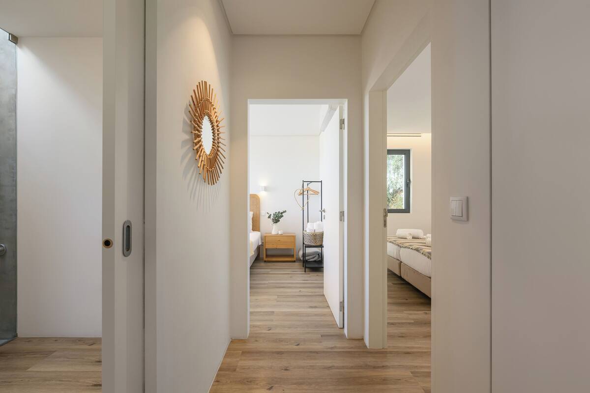 Ein Flur mit Holzboden, einer Wanddekoration und einem Bett mit Nachttisch im Hintergrund.