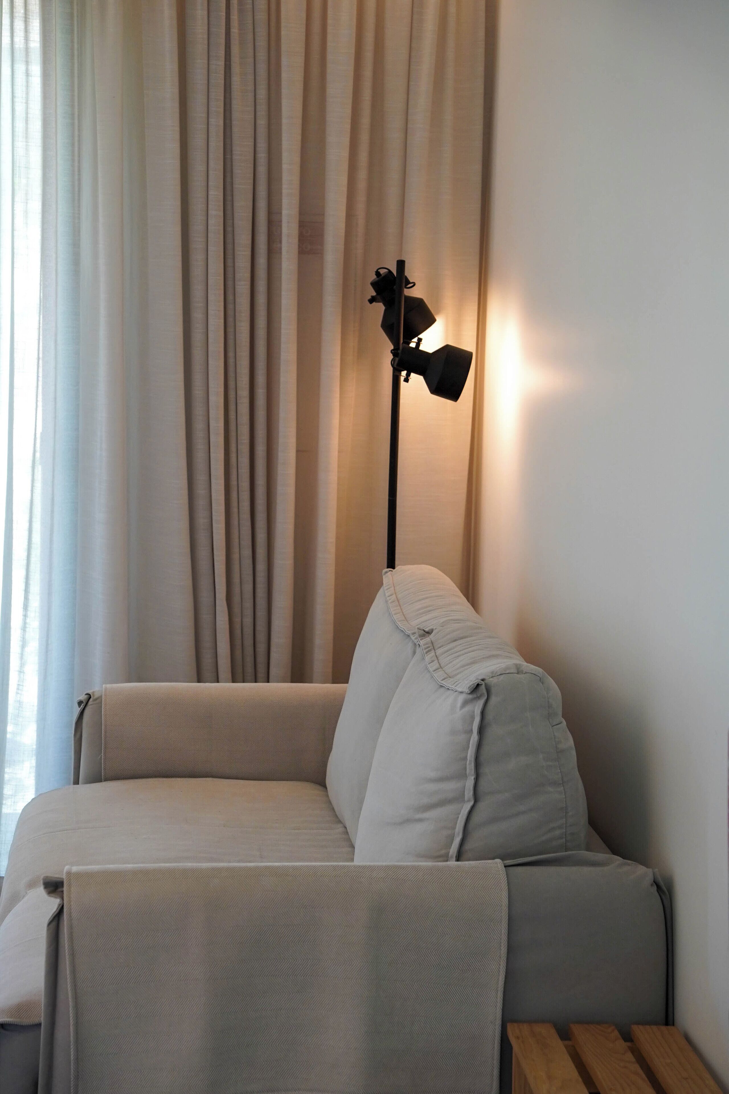 A sofa with a blanket, a floor lamp, and a window with curtains.