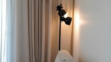 A sofa with a blanket, a floor lamp, and a window with curtains.