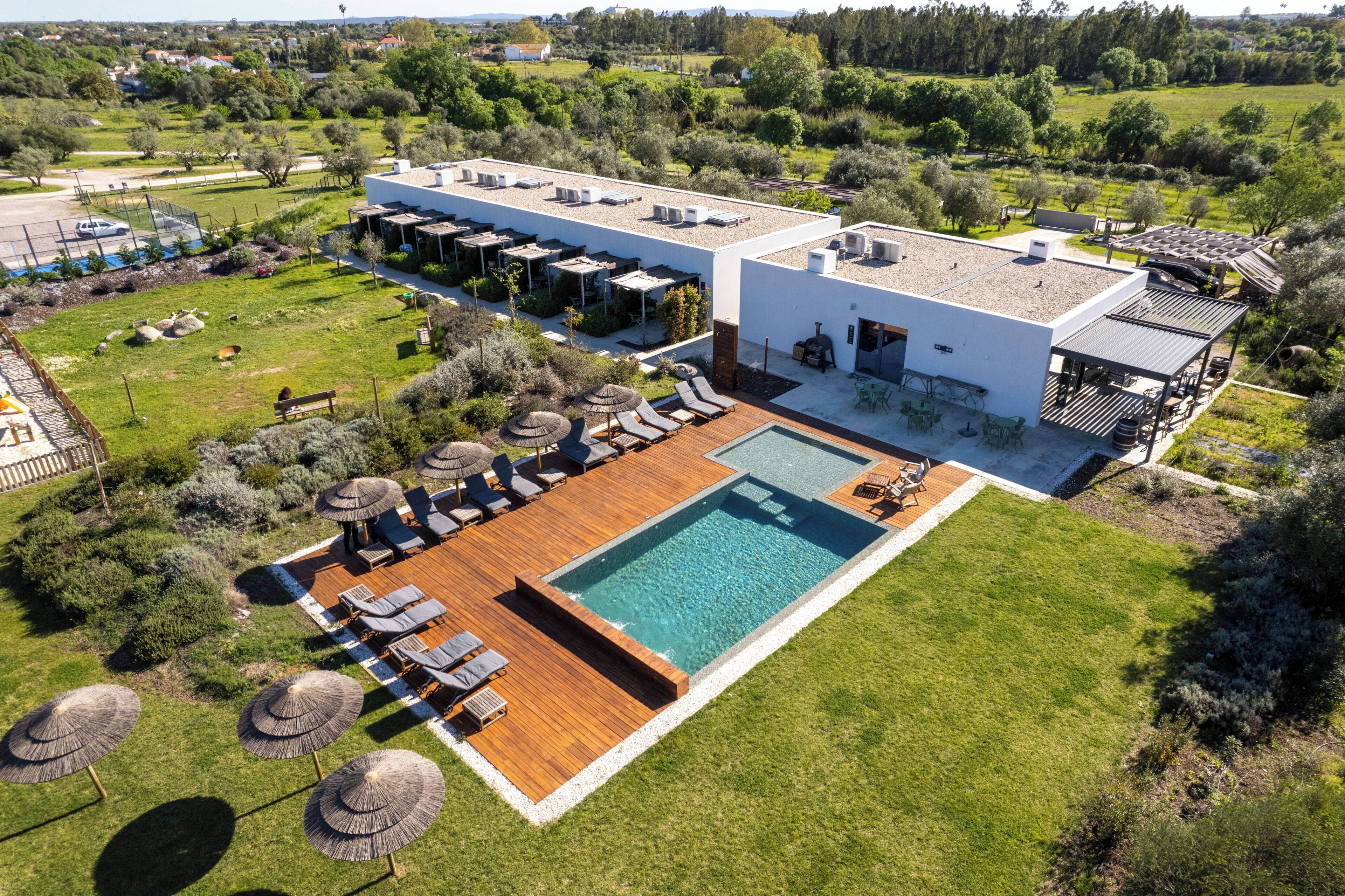 An aerial view of a modern hotel with a swimming pool, outdoor seating, and a garden.