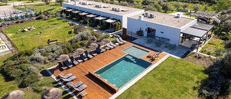 An aerial view of a modern hotel with a swimming pool, outdoor seating, and a garden.