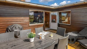 A wooden deck with a table and chairs, a grill, and a potted plant. - "Evelin" -  from the sea by Interhome (Hvide Sande)