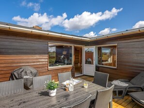 Un terrazzo in legno con tavolo e sedie, un barbecue e un vaso con una pianta.