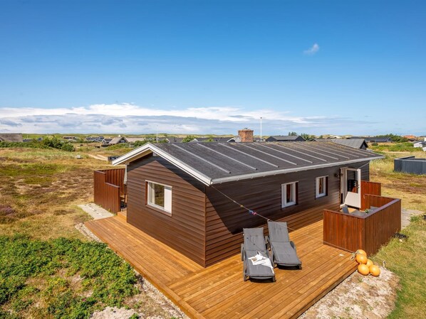 A modern house with a wooden deck, a small outdoor seating area, and a view of the surrounding landscape.