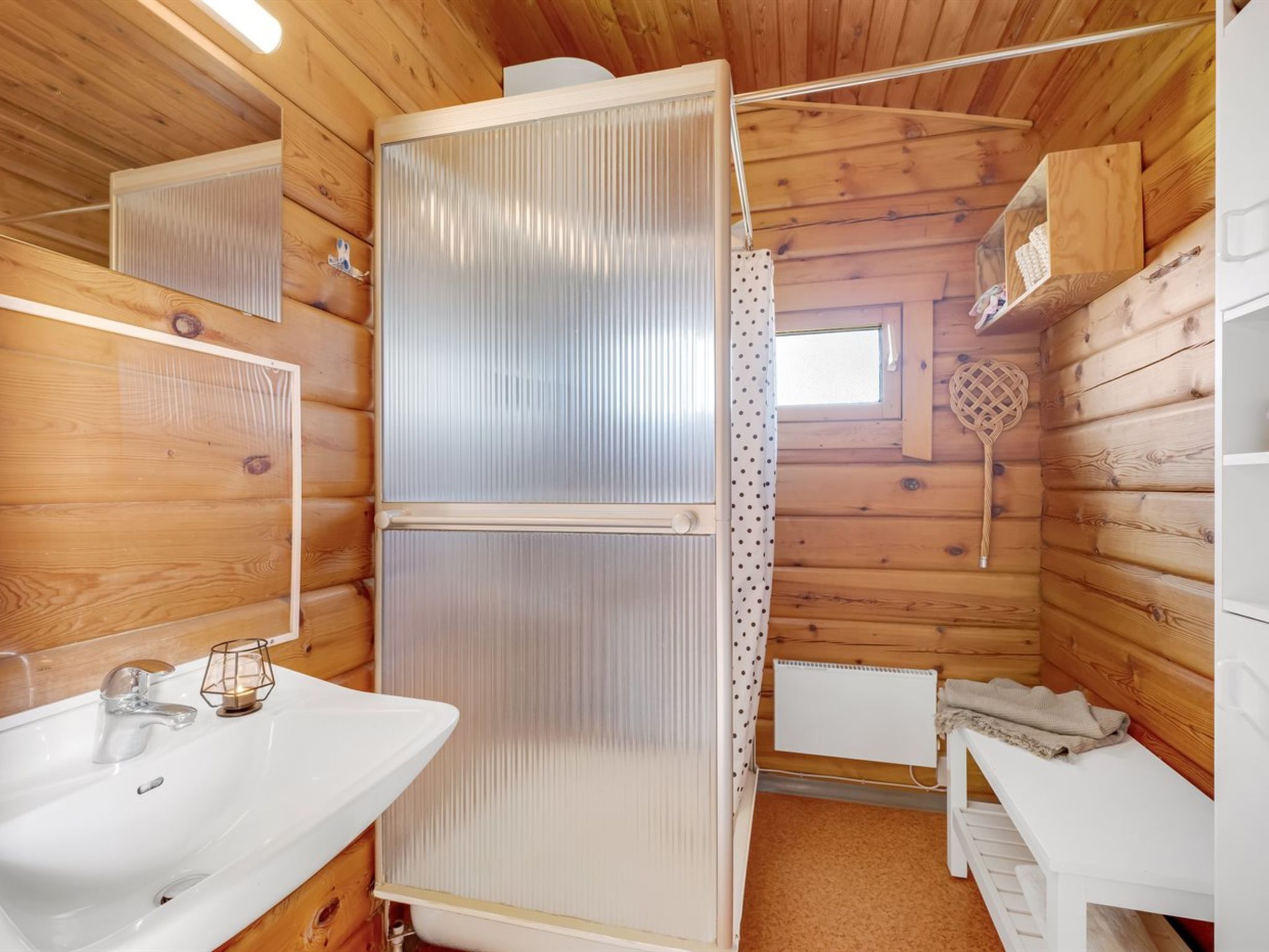 Ein Badezimmer einer Holzhütte mit einem weißen Waschbecken, einem Spiegel, einem Handtuchhalter und einer Duschkabine.