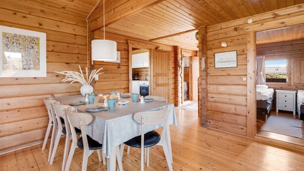 A wooden cabin interior with a dining area, kitchen, and a bedroom. - "Evelin" -  from the sea by Interhome (Hvide Sande)