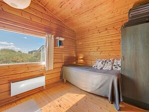 Camera da letto in una baita di legno, con un letto, una finestra e un termosifone.