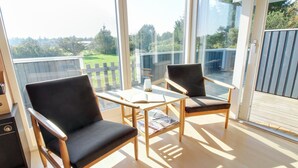 A balcony with two chairs and a table, large glass doors, and a view of greenery.