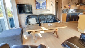 A modern living room with a wooden table, leather sofa, and a TV mounted on the wall.