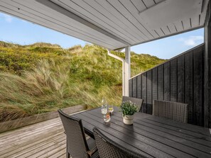 Una terraza de madera con mesa y sillas, con vistas a un paisaje cubierto de césped.