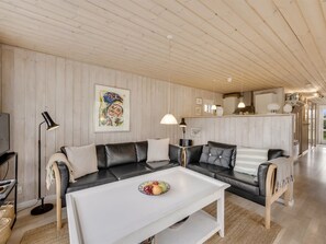 Un salón moderno con una mesa baja blanca, sofás de cuero negro y techo de madera.
