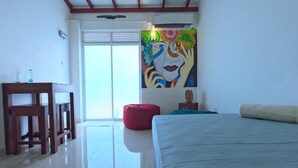 A bedroom with a bed, a desk, a chair, a red bean bag, and a colorful mural on the wall. - Unwind Restaurant & Hostel (Seeduwa - Katunayake)
