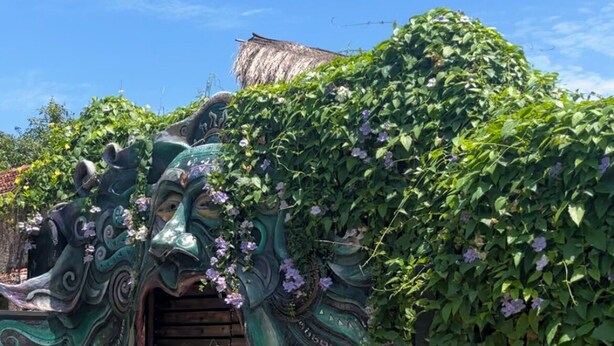 A building entrance with a decorative gate and a thatched roof structure in the background. - Unwind Restaurant & Hostel (Seeduwa - Katunayake)