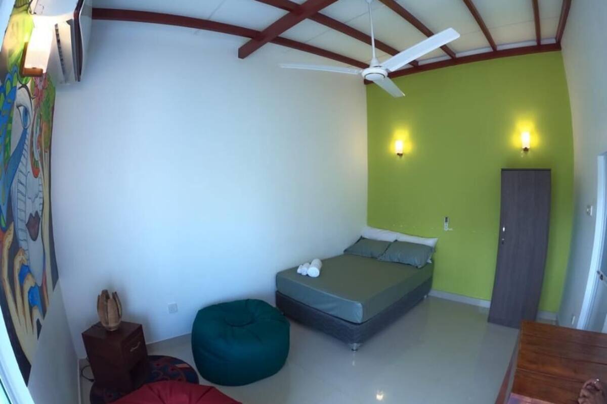 Ein Schlafzimmer mit einem Bett, einem Deckenventilator, einer grünen Wand und einer Tür.