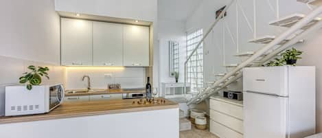 A modern kitchen with white cabinets, a microwave, a sink, and a refrigerator.